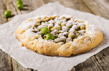 Gooseberry rustic tart on rough wooden background. Galette or crostata with fresh berries. Selective focus 