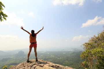 cheering woman hiker open arms on mountain peak