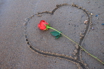 Red rose laying in a drawn heart in the sand.