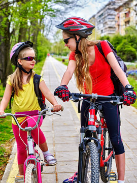 Bikes bicyclist girl. Girls wearing bicycle helmet and glass with rucksack ciclyng bicycle. Girls children cycling on yellow bike lane. Bicycle girl talk each other.