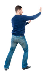 back view of business man pushes wall. Isolated over white background. Rear view people collection. backside view of person. bearded man in blue pullover shoves something on the side.