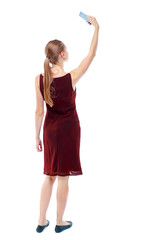 back view of standing young beautiful  woman  using a mobile phone. girl  watching. Rear view people collection.  backside view of person.  Isolated over white background. The girl in the maroon