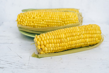 Bright yellow sweet corn on green plate on white painted wooden table