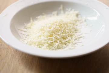 grated parmigiano in white plate over wood table