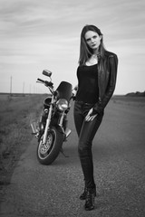 Fototapeta na wymiar Biker girl in a leather jacket posing near motorcycle