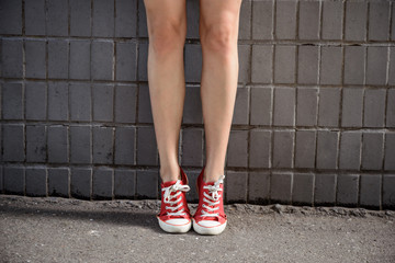 Close up of girl's legs in keds over grey wall.