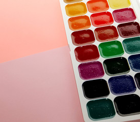 watercolor paints with brushes on a pink background, top view