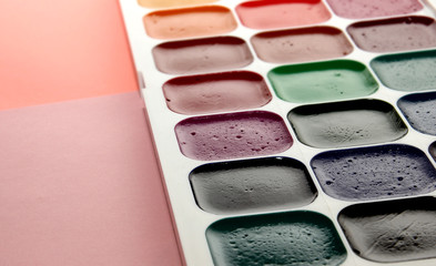 watercolor paints with brushes on a pink background, top view