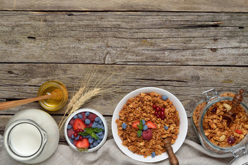 Ingredients for a healthy breakfast - berries, homemade granola, milk, honey on wooden table. Copyspace background.Top view.