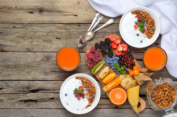 Ingredients for a healthy breakfast - berries, fruits, muesli, yogurt, juice on wooden table. Copyspace background.Top view.