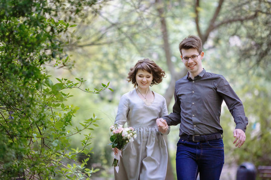 Happy couple walks holding their hands together under green tree