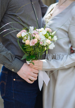 Groom in jeans and bride in grey dress hold  wedding bouquet in