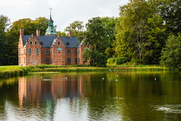 Bath House hunting lodge reflected on the lake water near Frederiksborg castle in Copenhagen, Denmark. Romantic park around lonely pond with water birds.