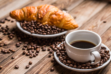 Breakfast coffee - cup, sugar, milk jug and croissant with coffee beans.