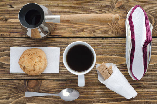 Cup of coffee on a wooden table, sugar, spoon, biscuits, napkins, top view