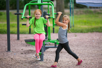 Two little fun girls is engaged in sports equipment outdoor.