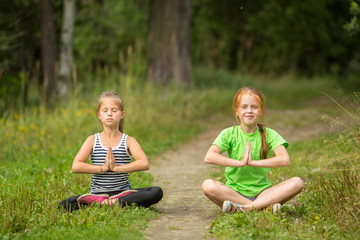 Fototapeta premium Two fun little girls sitting in yoga meditation outdoors.