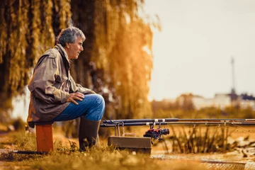 Fototapeten Senior man fishing on a freshwater lake sitting patiently © Mediteraneo