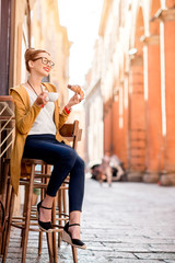 Fototapeta na wymiar Young woman having italian breakfast with croissant and coffee at the cafe on the street in Bologna city. Soft focus with small depth of field