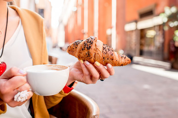 Female hands holding croissant and coffee, traditional italian breakfast at the cafe in Bologna...