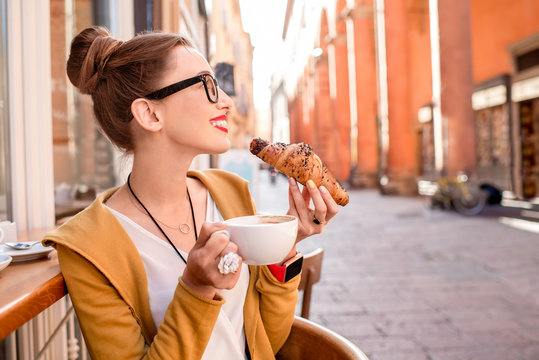 Fototapeta Young woman having italian breakfast with croissant and coffee at the cafe on the street in Bologna city. Soft focus with small depth of field