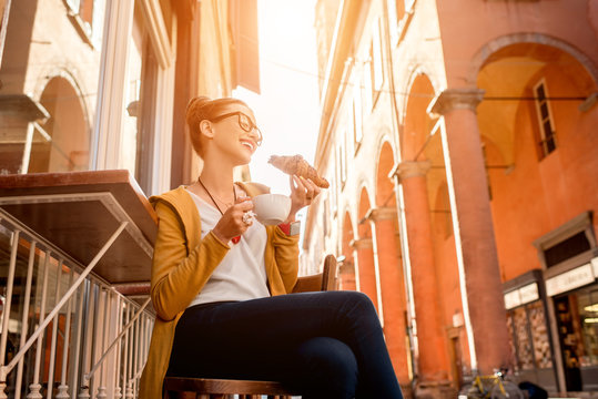 Fototapeta Young woman having italian breakfast with croissant and coffee at the cafe on the street in Bologna city. Soft focus with small depth of field