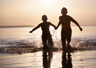 Fototapeta premium Children run along the water at sunset