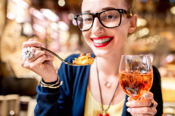 Young woman eating tortellini pasta in front of the food shop in Bologna. Tortellini ring-shaped pasta was invented in Bologna.