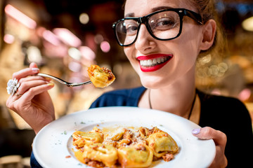 Young woman eating tortellini pasta in front of the food shop in Bologna. Tortellini ring-shaped...