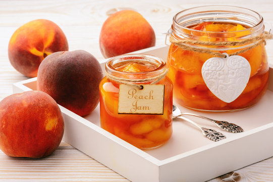 Peach jam in glass jars on white wooden background.