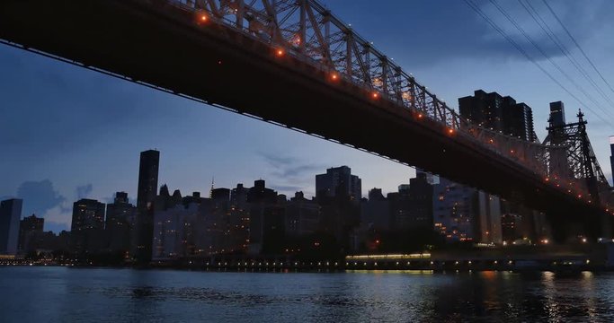 An evening or dusk establishing shot of the Manhattan skyline as seen from under the Ed Koch Queensboro Bridge.  	