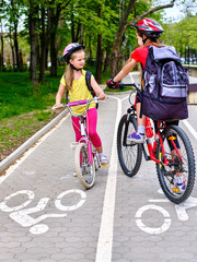Fototapeta premium Bicycle girls wearing bicycle helmet and glass with rucksack ride on bicycle. Girls children cycling meet on white bike lane. Bike share program save money and time at city street.