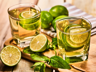 Country alcohol cocktail. On wooden boards are two glasses with green transparent drink and half lime . A drink number one hundred eighty six mojito with mint leaf . Country life. Boards background.