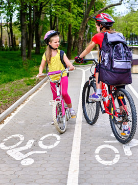Bicycle girls wearing bicycle helmet and glass with rucksack ride on bicycle. Girls children cycling meet on white bike lane. Bike share program save money and time at city street.