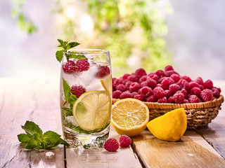 On wooden boards glass with raspberry alcohol cocktail and ice cubes. Cocktail number hundred and ninety six cocktail raspberry mojito with raspberry basket. Country life. Outdoor background.