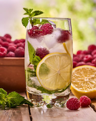 On wooden boards glass with raspberry alcohol cocktail and ice cubes. Cocktail number hundred and ninety seven cocktail raspberry mojito with raspberry bowl. Country outdoor background.