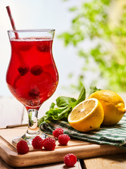On wooden boards is ice cold beverage glass with raspberry cocktail . Alcohol country cocktail beverage number two hundred six and two with leaf mint and lemon. Outdoor country cocktail .