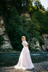 Tender bride touches her shoulder while posing by the mountain r