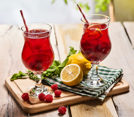 On wooden boards are ice cold beverage two glasses with red berries lemon cocktail . Alcohol country cocktail beverage number three hundred and sixteen with leaf mint. Outdoor cocktail . Sun morning.