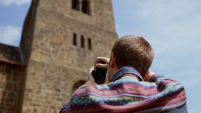 Young man photographing church on mirrorless camera