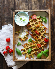 Zucchini waffles with fresh tomatoes, basil and yogurt sauce on a wooden background, overhead shot