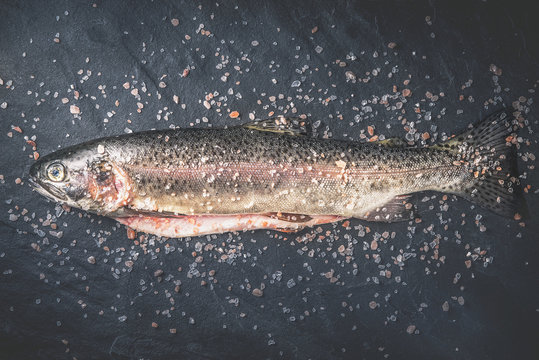 Raw trout  with salt on the dark stone background top view