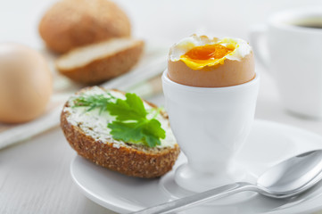 Perfect soft boiled egg, open bread sandwich with butter and cup of coffee on a table. Traditional food for healthy breakfast.
