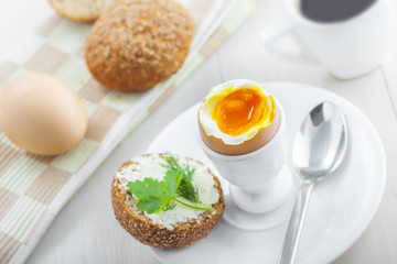 Traditional breakfast with perfect soft boiled egg, sandwich with butter and dill, coffee cup on a table. International cuisine food.