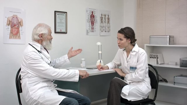 Old doctor talking to young female doctor.