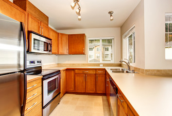 Empty kitchen room interior with wooden cabinets and tile floor.