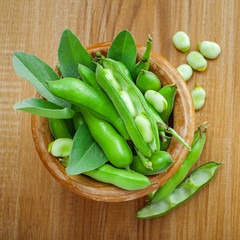 Bowl of podded green broad beans on a wooden table. Healthy organic food. Top view.