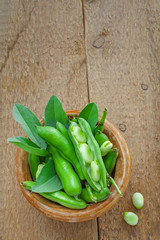 Fresh green broad beans in a bowl. Fresh raw vegetables on a wooden table. Ingredients healthy vegetarian food. Top view.