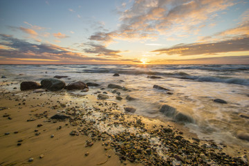 Sea landscape at sunset, sandy beach and cliff,waves breaking on the shore

