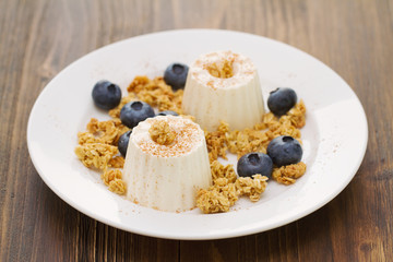 fresh cheese with granola and blueberries on plate on brown wooden background